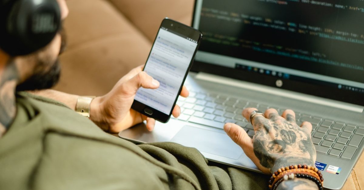 young man looking at mobile phone and laptop open